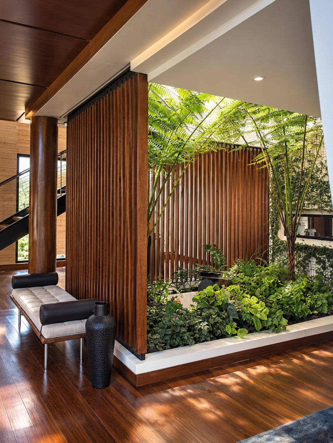 Atrio con divisiones de listones en madera junto a un jardín interior.