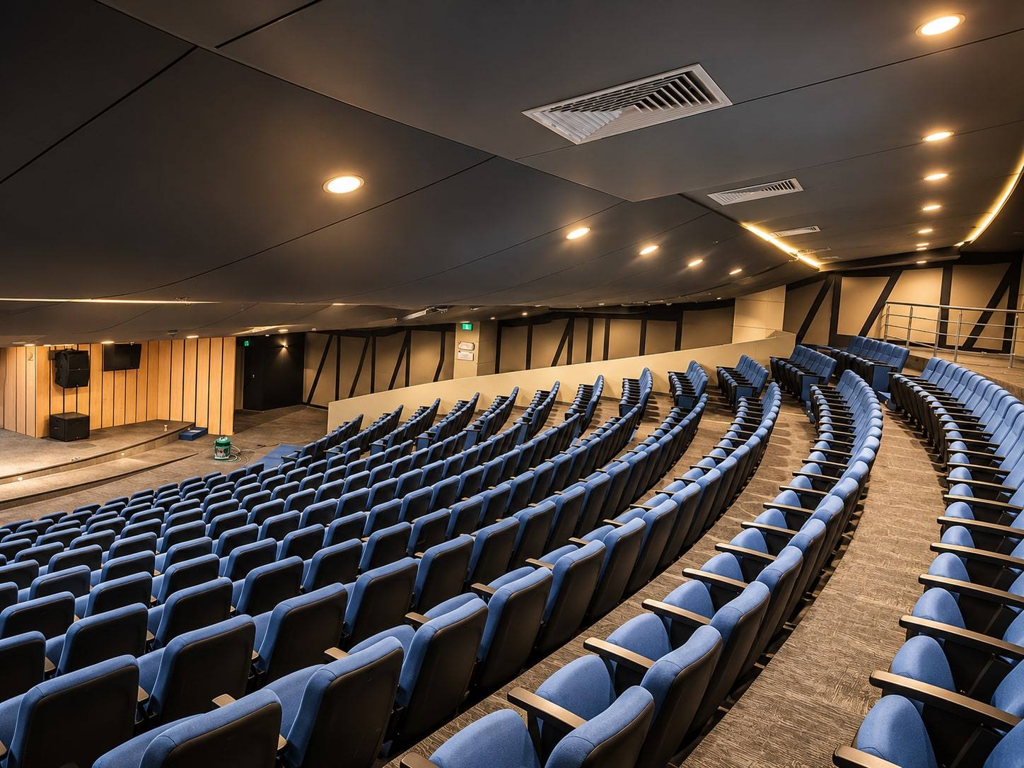 Auditorio con butacas azules en curva y muros de madera.