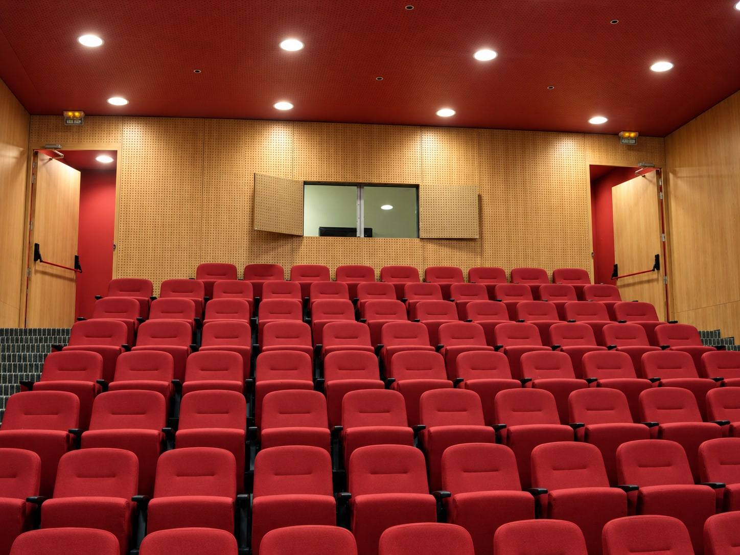 Auditorio con butacas rojas y muro de paneles de madera.