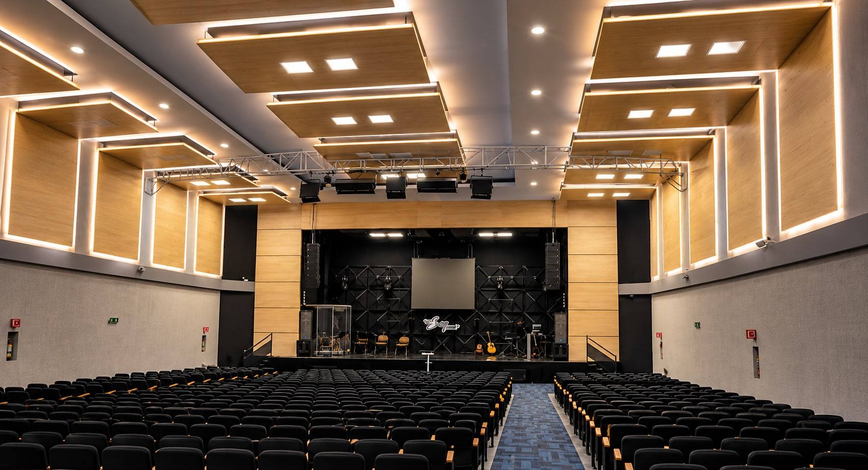 Auditorio con escenario y paneles de madera iluminados.